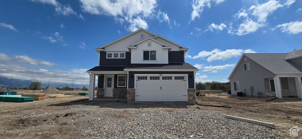 View of front of house with an attached garage, cooling unit, stone siding, and driveway