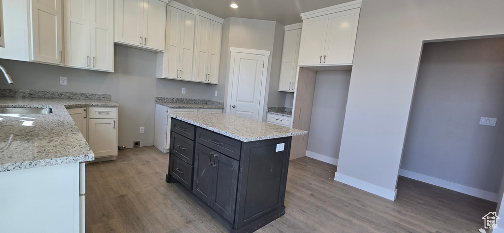 Kitchen with white cabinetry, a kitchen island, wood finished floors, and a sink