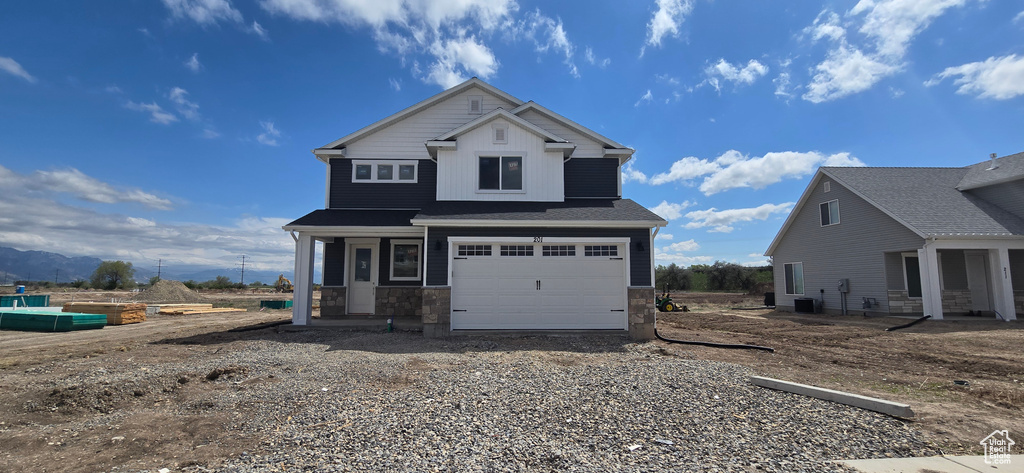View of front of house featuring an attached garage, stone siding, and gravel driveway