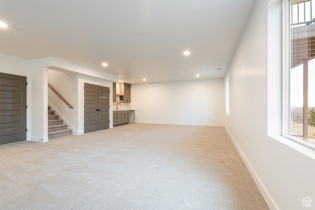 Below grade area featuring baseboards, stairway, light carpet, recessed lighting, and a sink
