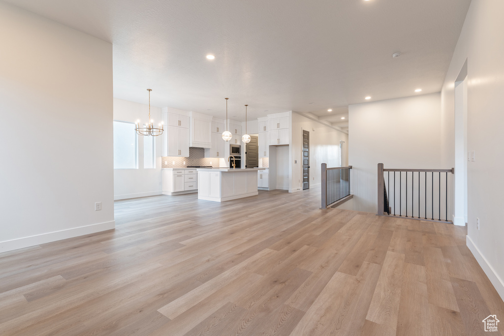 Unfurnished living room featuring a notable chandelier, recessed lighting, baseboards, and light wood-style floors