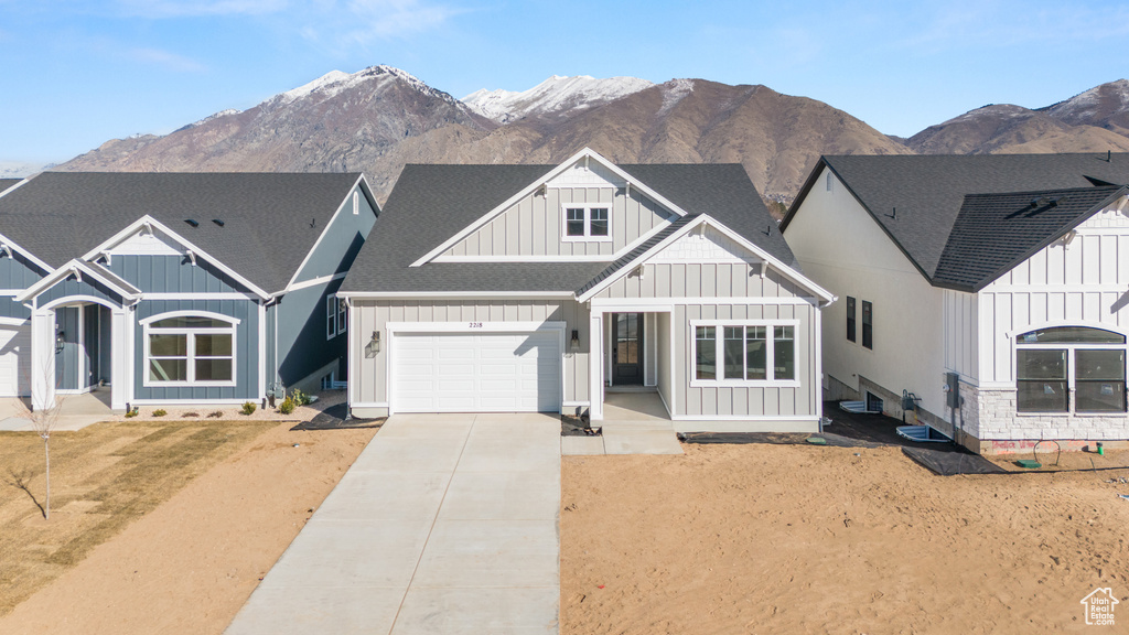 View of front of house with board and batten siding, roof with shingles, driveway, a garage, and a mountain view