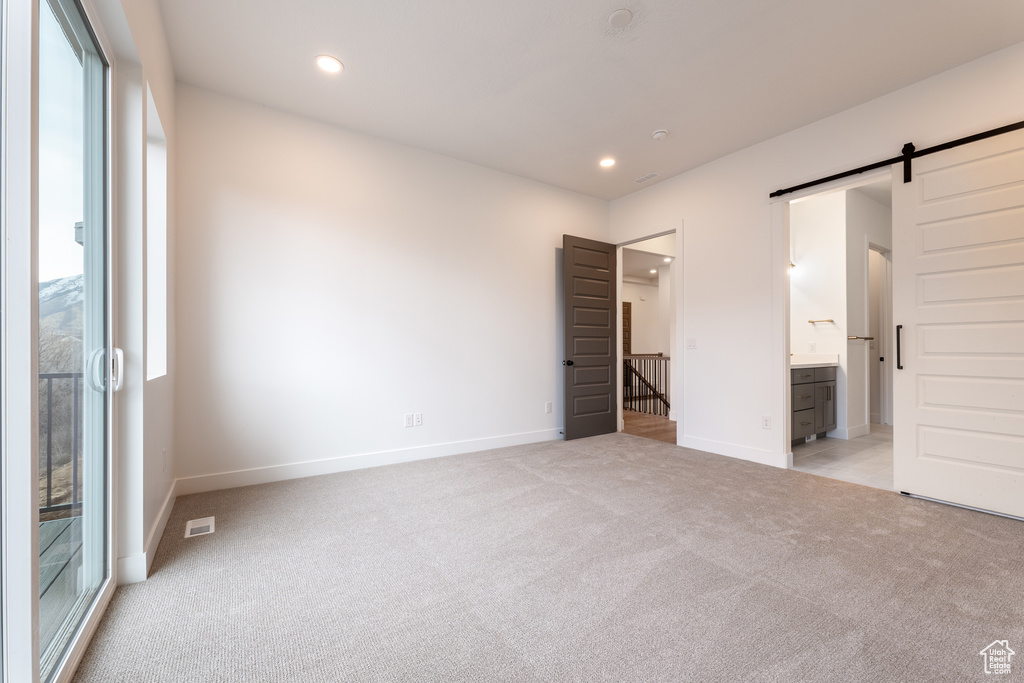 Unfurnished bedroom with visible vents, baseboards, recessed lighting, light carpet, and a barn door