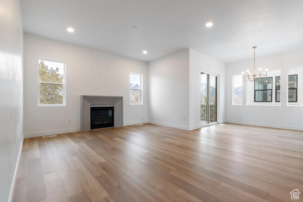 Unfurnished living room with baseboards, a glass covered fireplace, recessed lighting, light wood-style floors, and a notable chandelier