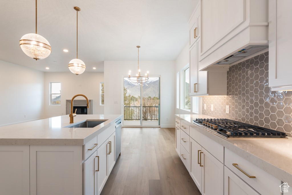 Kitchen with light wood-style flooring, a sink, decorative backsplash, dishwasher, and stainless steel gas cooktop