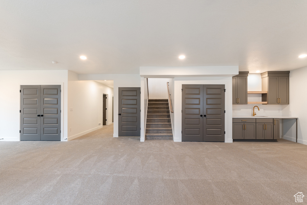 Unfurnished living room with stairs, recessed lighting, light colored carpet, and a sink