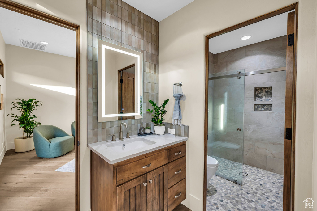 Full bathroom with visible vents, backsplash, toilet, a stall shower, and wood finished floors