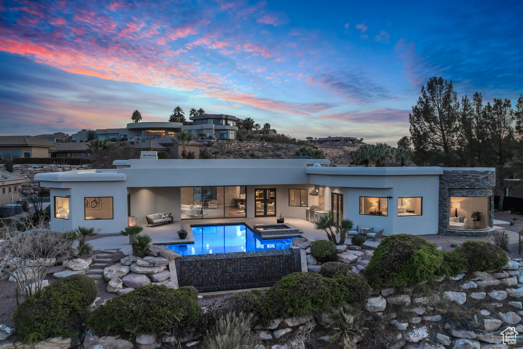 Rear view of house with stucco siding, stone siding, a patio, an outdoor pool, and an in ground hot tub