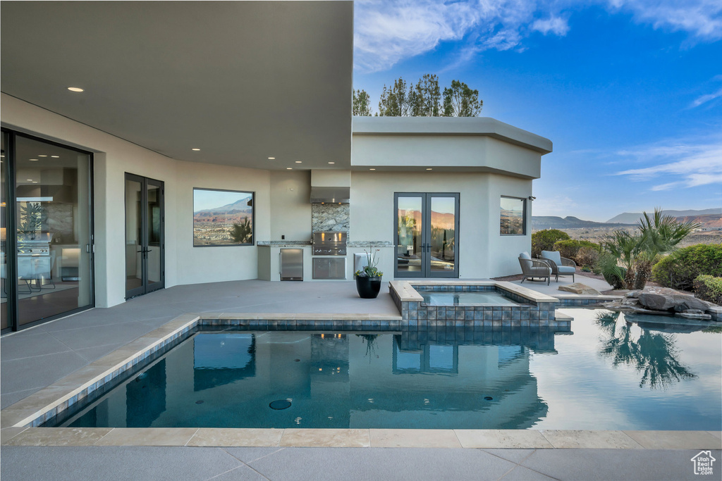 View of pool with a pool with connected hot tub, exterior kitchen, french doors, a mountain view, and a patio