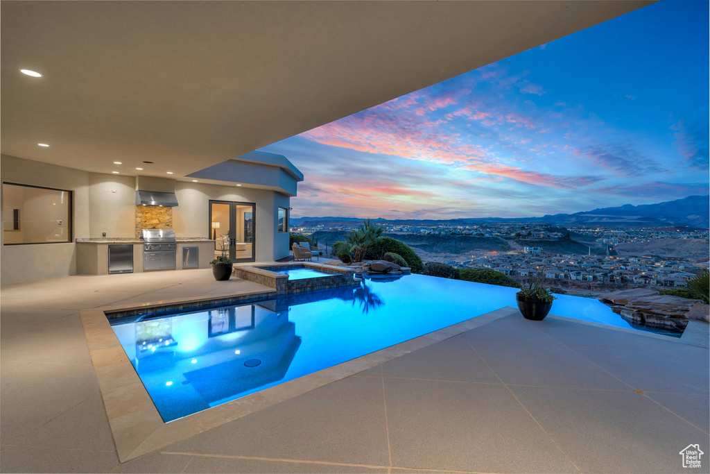 Pool at dusk with a patio, area for grilling, a mountain view, and a pool with connected hot tub