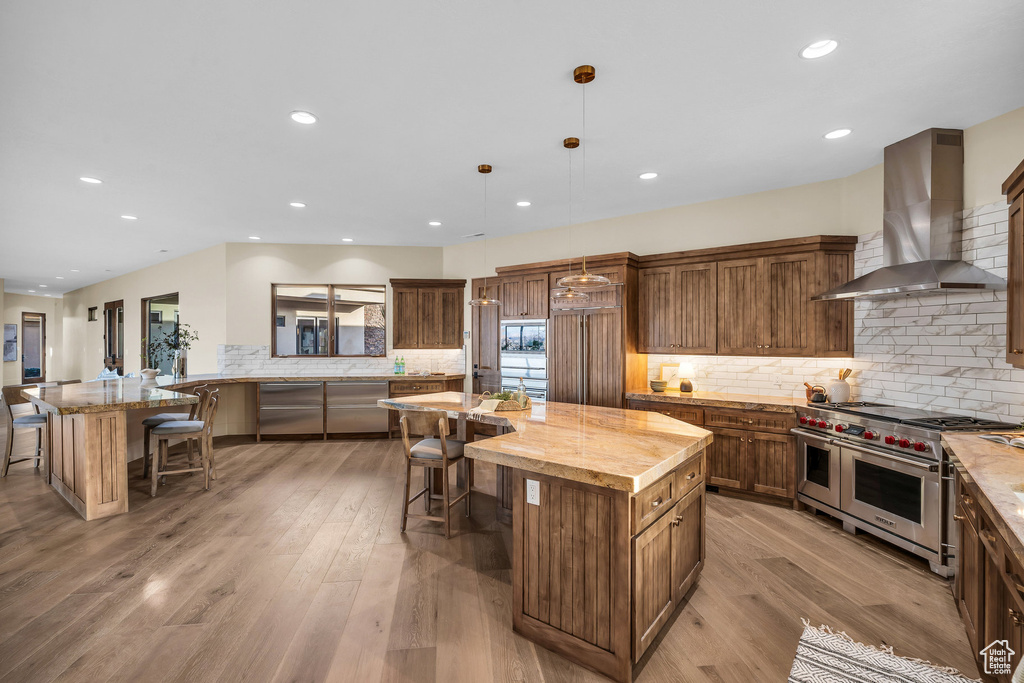 Kitchen featuring light wood-type flooring, double oven range, a kitchen breakfast bar, and wall chimney exhaust hood