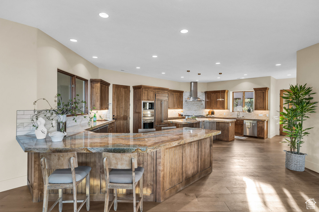 Kitchen with dark wood-style floors, a kitchen island, a sink, stainless steel appliances, and wall chimney range hood