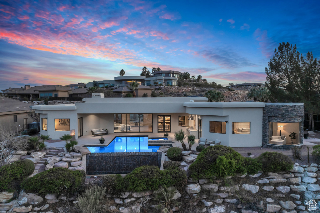 Back of property at dusk with an outdoor living space, stucco siding, a patio, and an outdoor pool