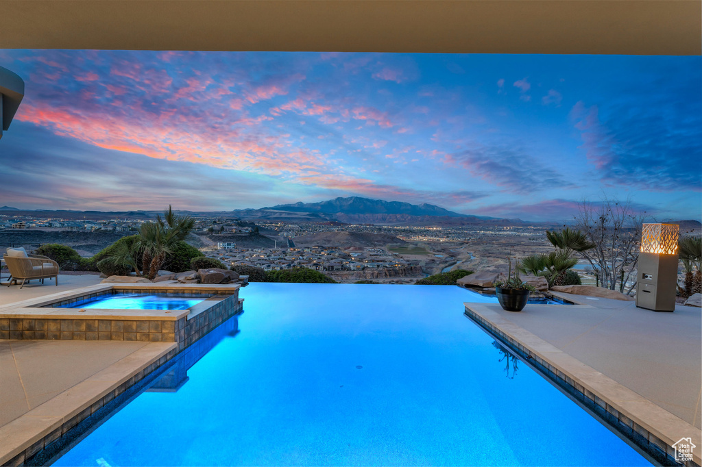 Pool at dusk with a mountain view and a pool with connected hot tub
