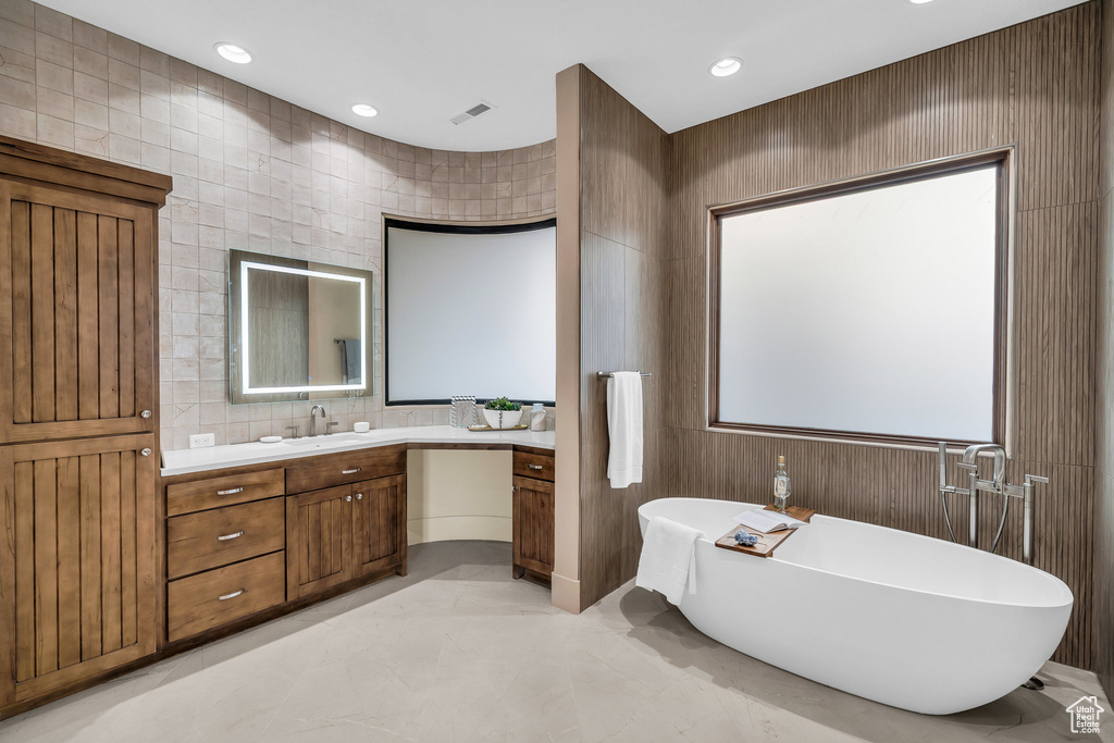 Full bathroom featuring vanity, visible vents, recessed lighting, a freestanding bath, and tile walls