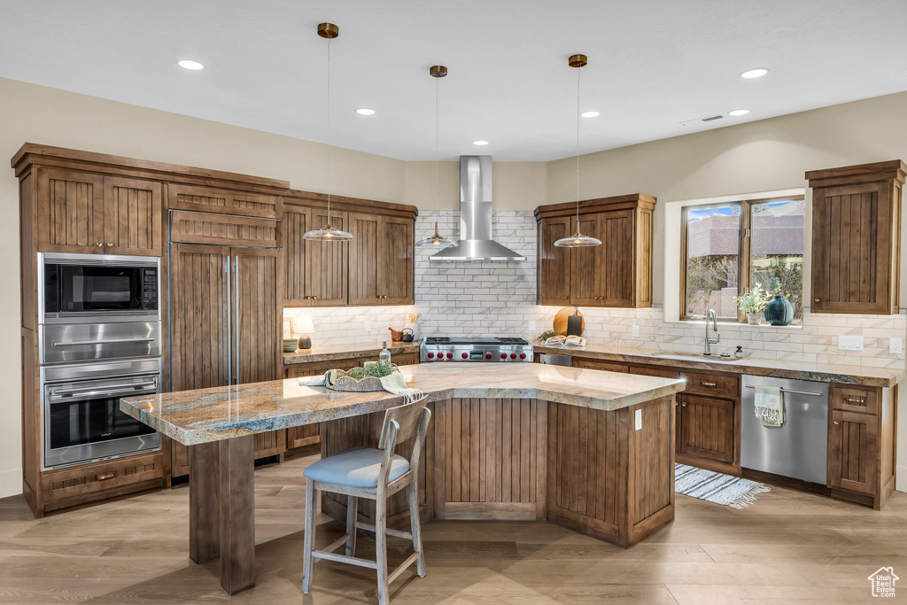 Kitchen with a kitchen island, wall chimney range hood, decorative backsplash, appliances with stainless steel finishes, and a sink