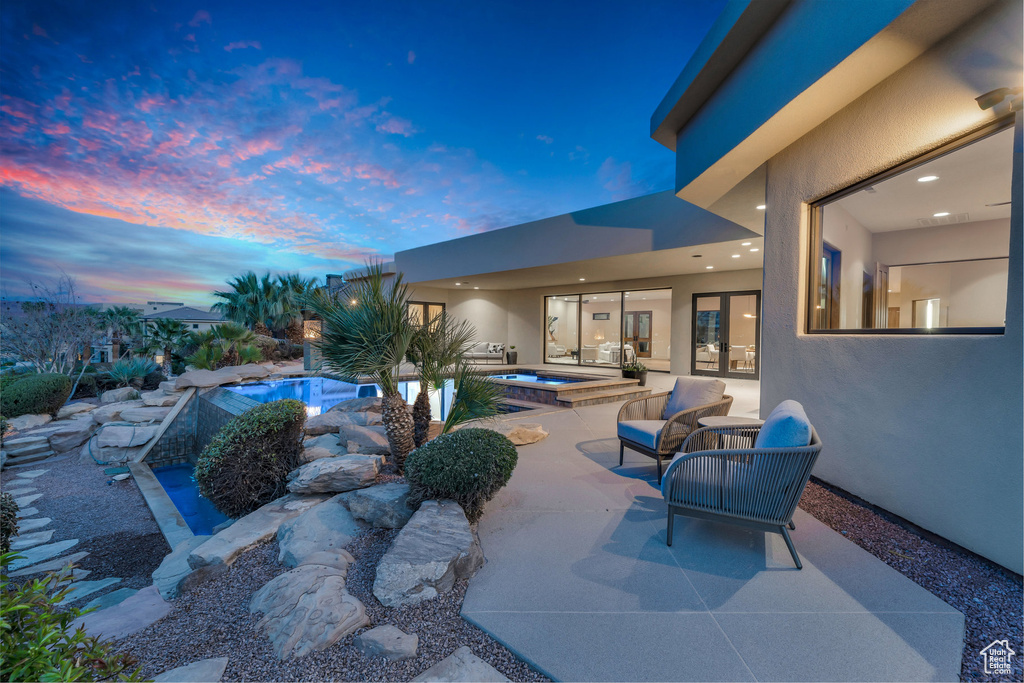 Pool at dusk featuring an in ground hot tub, an outdoor pool, and a patio