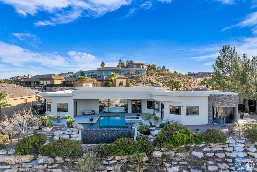 Rear view of house featuring stone siding, stucco siding, an outdoor pool, and a patio