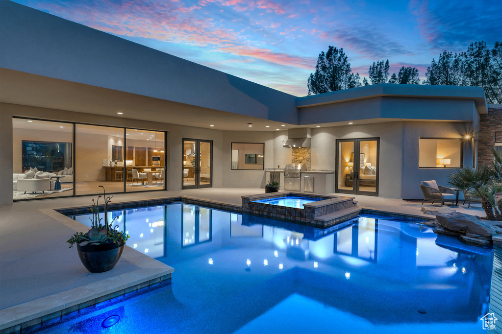 Pool at dusk featuring a patio area, an outdoor kitchen, and french doors