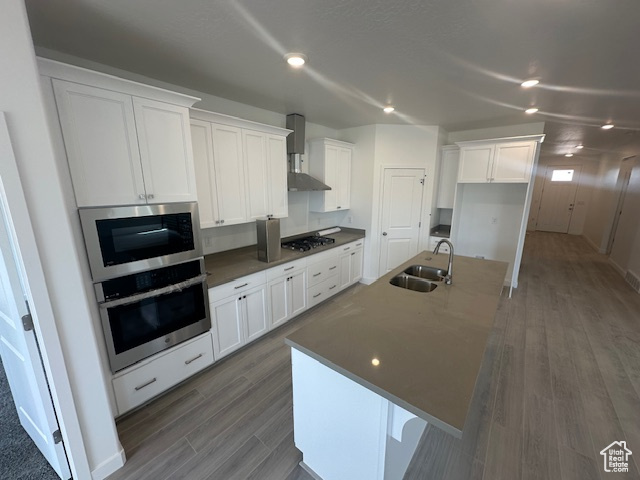 Kitchen with white cabinets, a sink, a kitchen island with sink, stainless steel oven, and wall oven