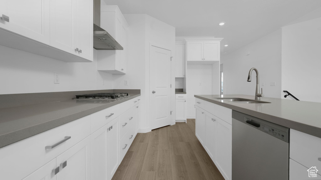 Kitchen with dishwasher, a sink, wall chimney range hood, wood finished floors, and recessed lighting