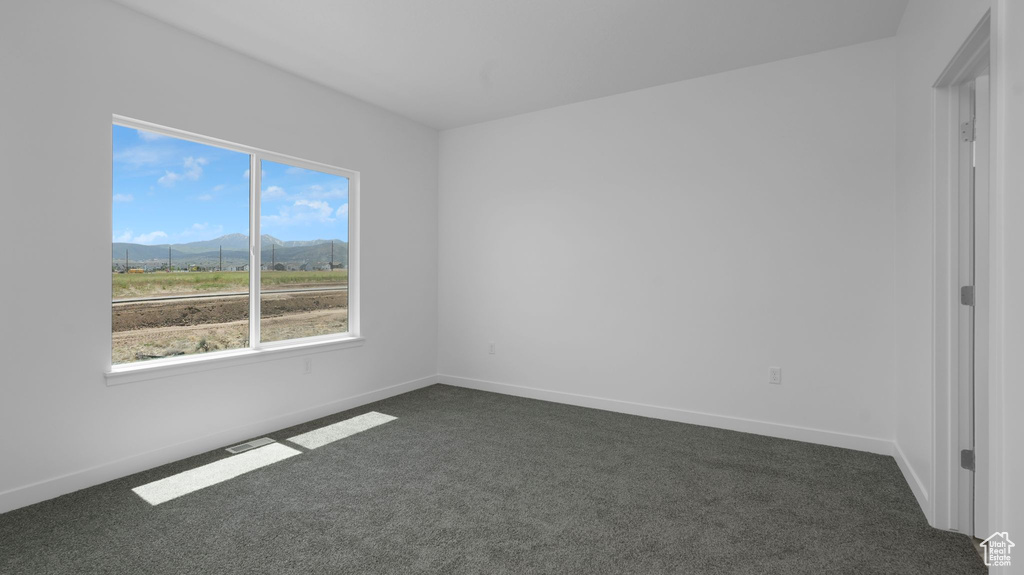 Empty room with a mountain view, dark colored carpet, healthy amount of natural light, and baseboards
