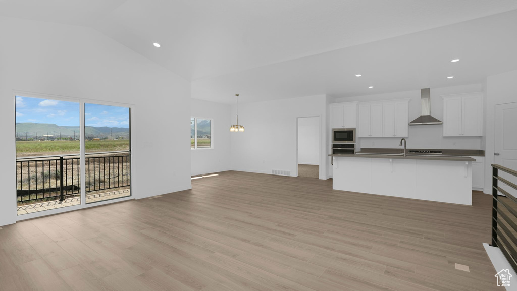 Unfurnished living room featuring recessed lighting, light wood-type flooring, a sink, high vaulted ceiling, and a chandelier