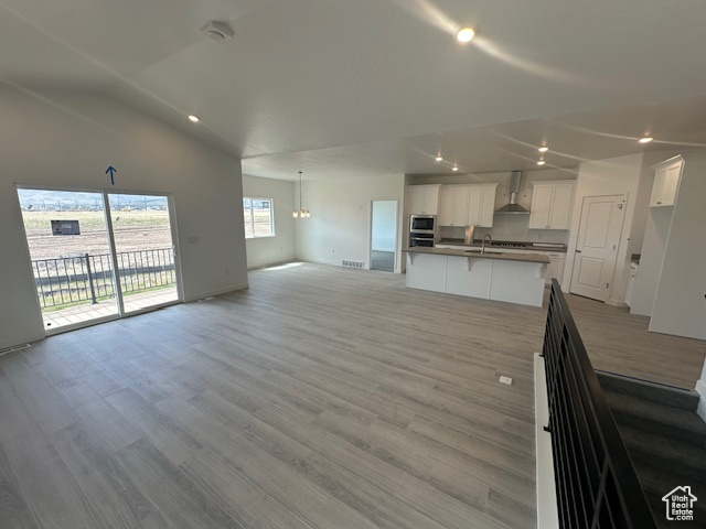 Unfurnished living room with a sink, light wood finished floors, recessed lighting, baseboards, and lofted ceiling