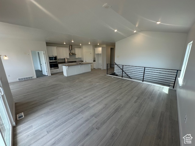 Unfurnished living room with baseboards, vaulted ceiling, visible vents, and light wood-type flooring