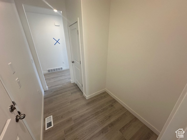 Hall with baseboards, visible vents, and wood finished floors