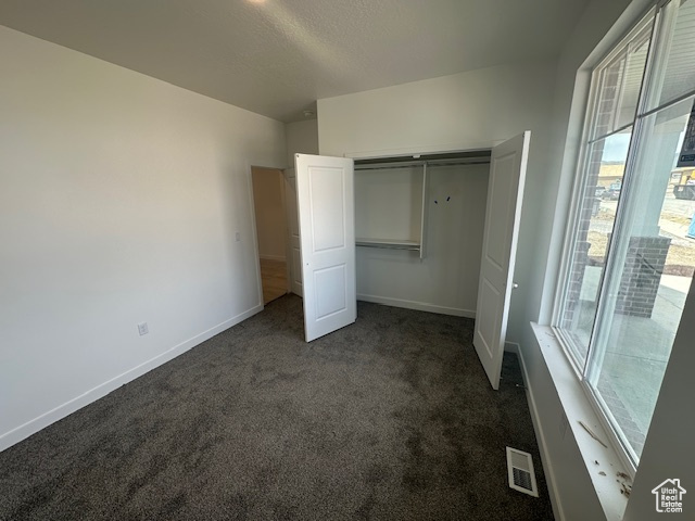 Unfurnished bedroom featuring baseboards, visible vents, dark carpet, and a closet