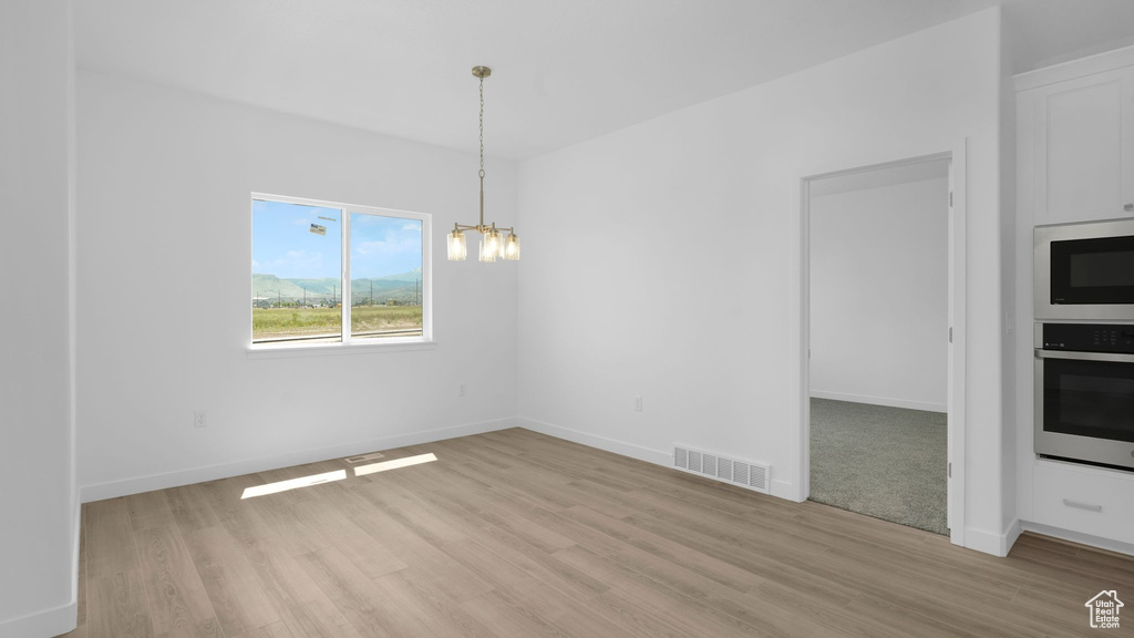 Unfurnished dining area with a chandelier, light wood-style floors, and baseboards