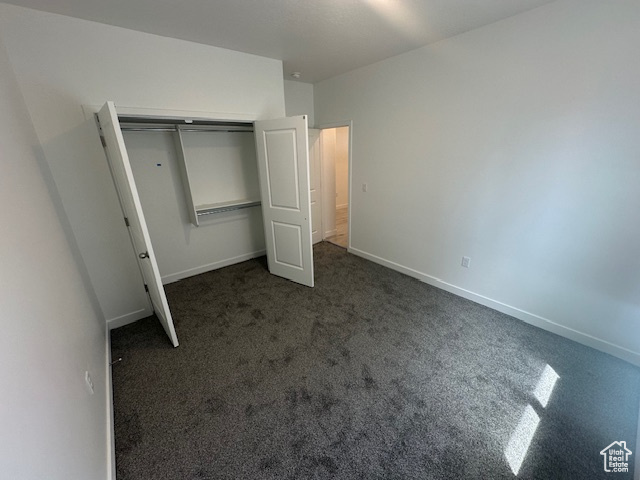Unfurnished bedroom with a closet, baseboards, and dark colored carpet