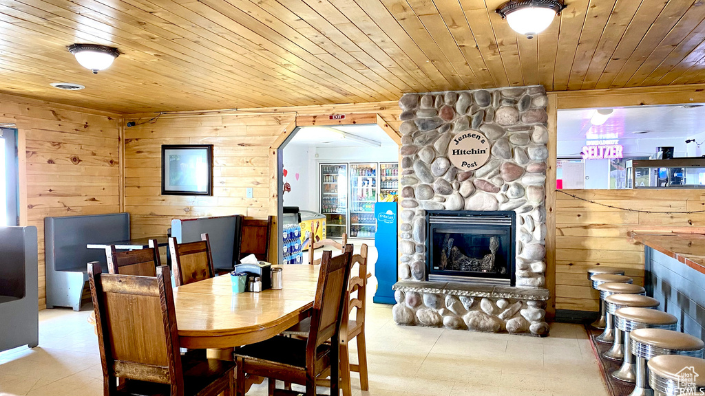 Dining room with a stone fireplace, wood ceiling, and wood walls