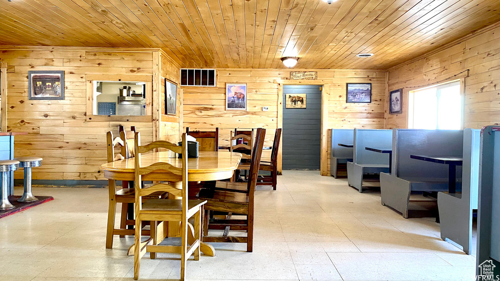 Dining space featuring wooden ceiling, light floors, visible vents, and wood walls