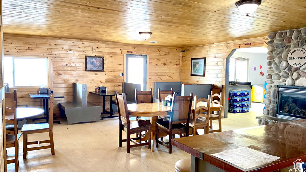 Dining room featuring arched walkways, wooden walls, a stone fireplace, wooden ceiling, and light floors
