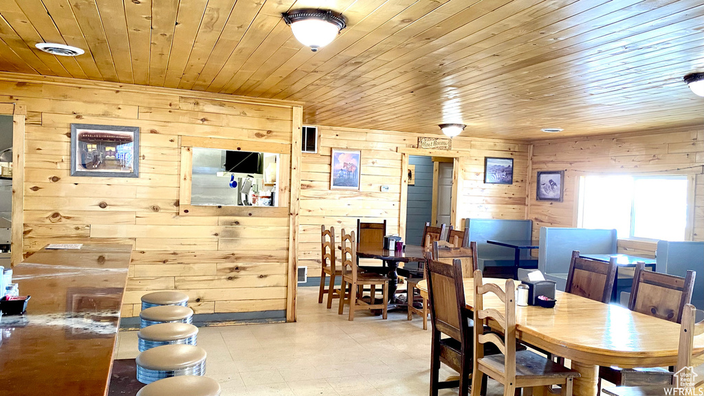 Dining space featuring tile patterned floors, visible vents, wooden ceiling, and wood walls