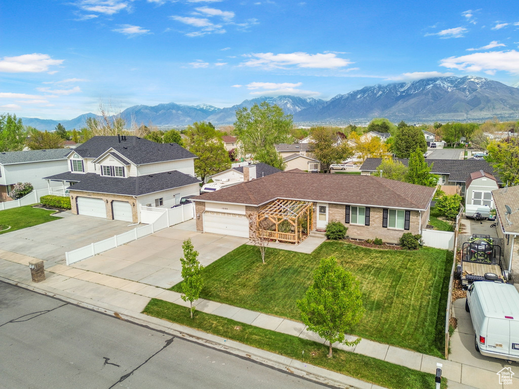 View of front of house featuring a front lawn, fence, brick siding, concrete driveway, and a mountain view