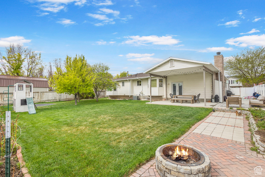 Back of house featuring an outdoor fire pit, a fenced backyard, a chimney, a lawn, and a patio