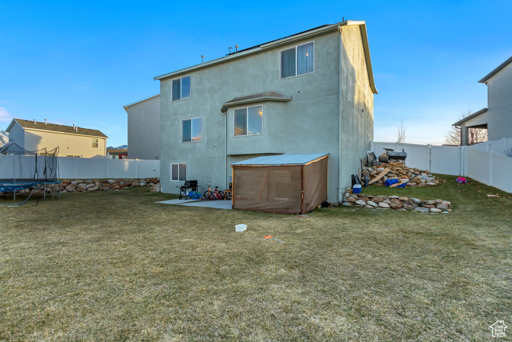 Back of house featuring a fenced backyard, a lawn, a trampoline, and stucco siding