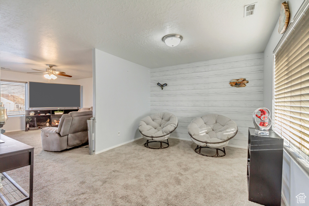 Sitting room featuring wooden walls, visible vents, baseboards, carpet, and a textured ceiling