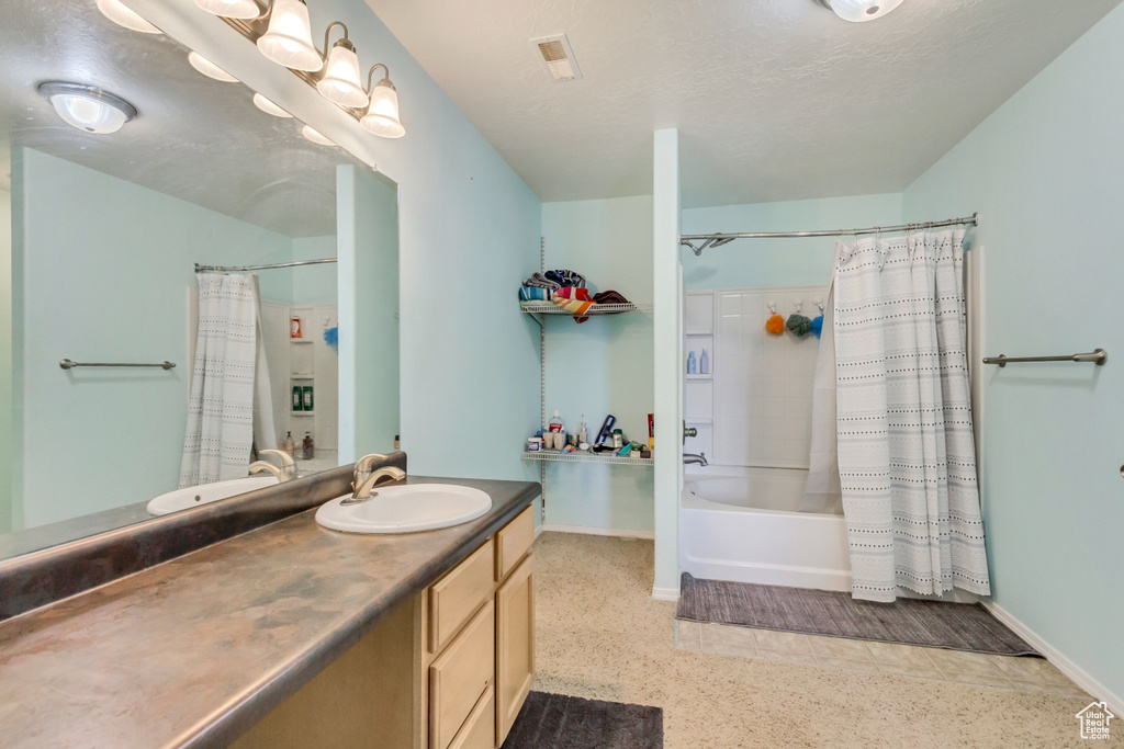 Full bathroom featuring shower / bathtub combination with curtain, a textured ceiling, speckled floor, baseboards, and vanity