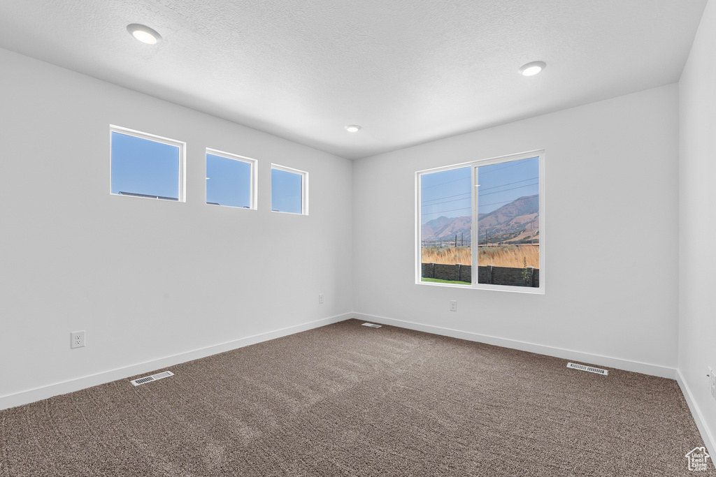 Unfurnished room with visible vents, plenty of natural light, baseboards, and dark carpet