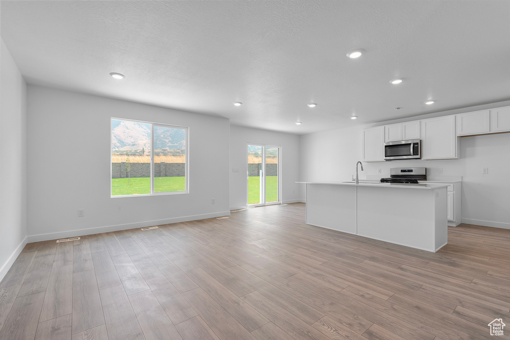 Kitchen featuring light wood-style flooring, a sink, open floor plan, white cabinetry, and appliances with stainless steel finishes