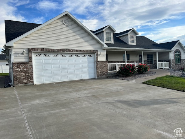 View of front of property with brick siding, a porch, driveway, and an attached garage