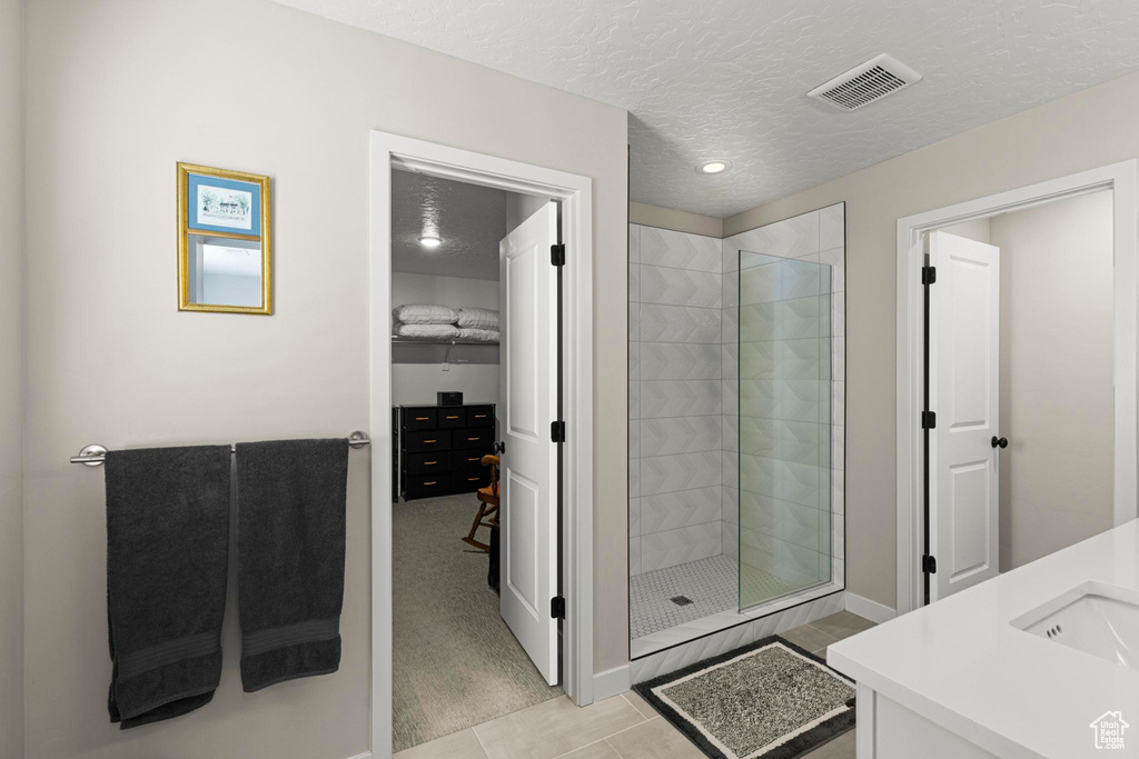 Bathroom with visible vents, a tile shower, tile patterned floors, a textured ceiling, and a sink
