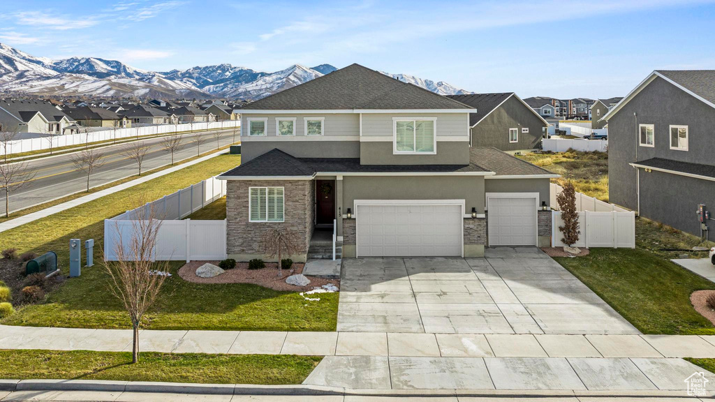 View of front facade with a shingled roof, fence, concrete driveway, a garage, and stone siding