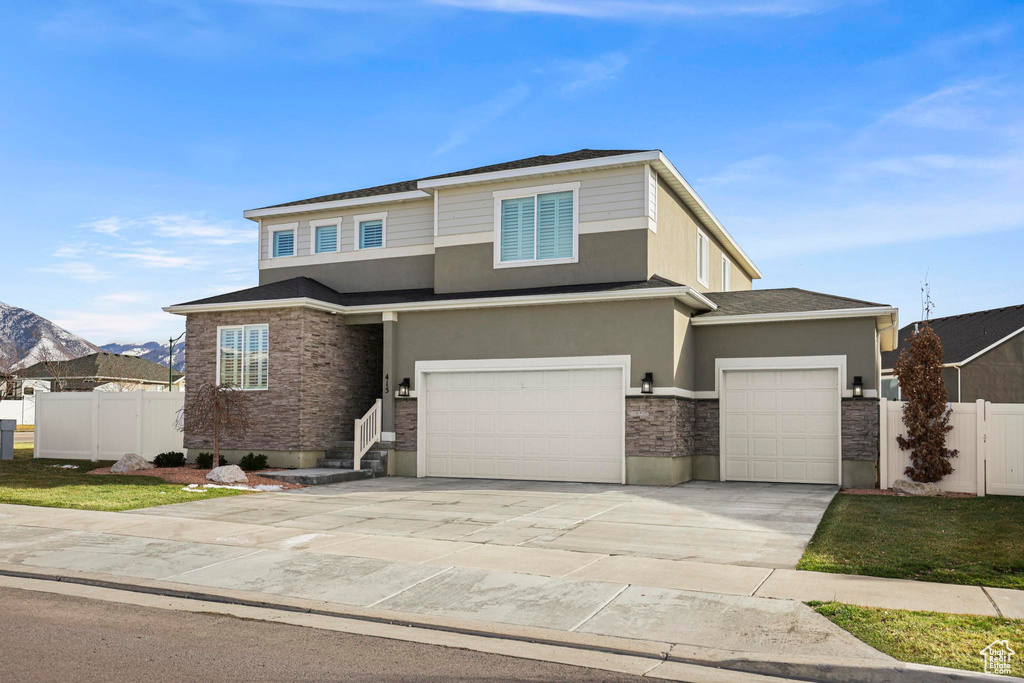View of front of home with stucco siding, stone siding, concrete driveway, and fence