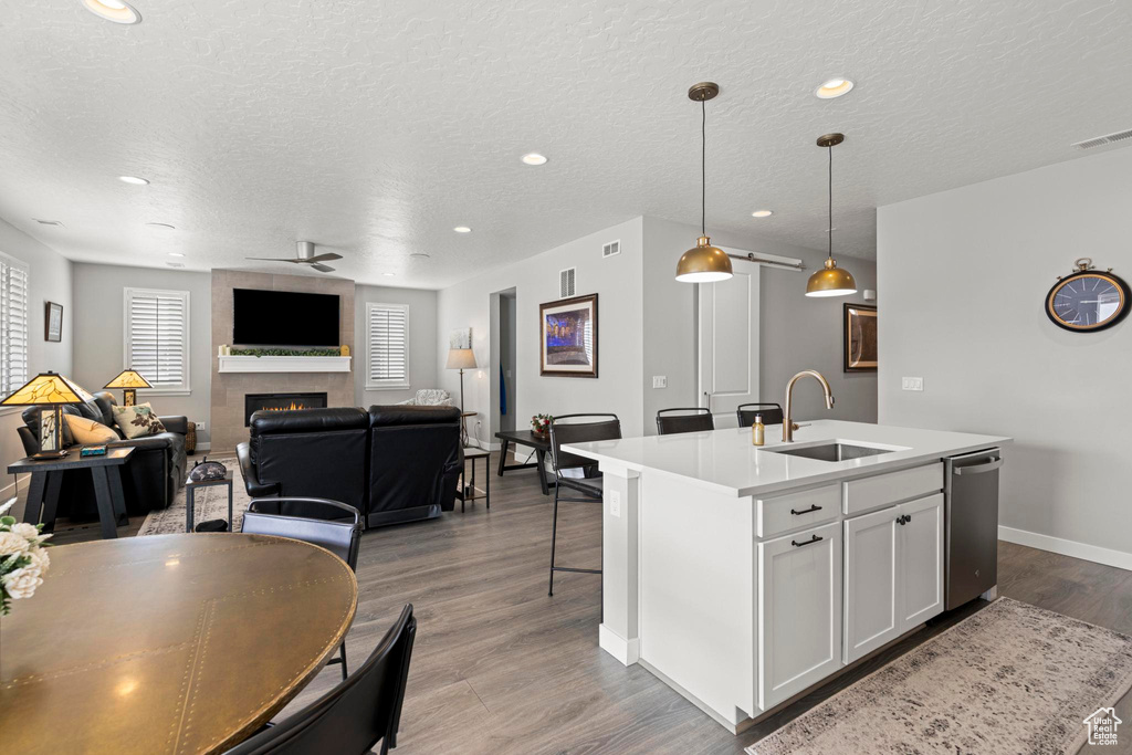 Kitchen featuring a ceiling fan, wood finished floors, a center island with sink, a fireplace, and a sink