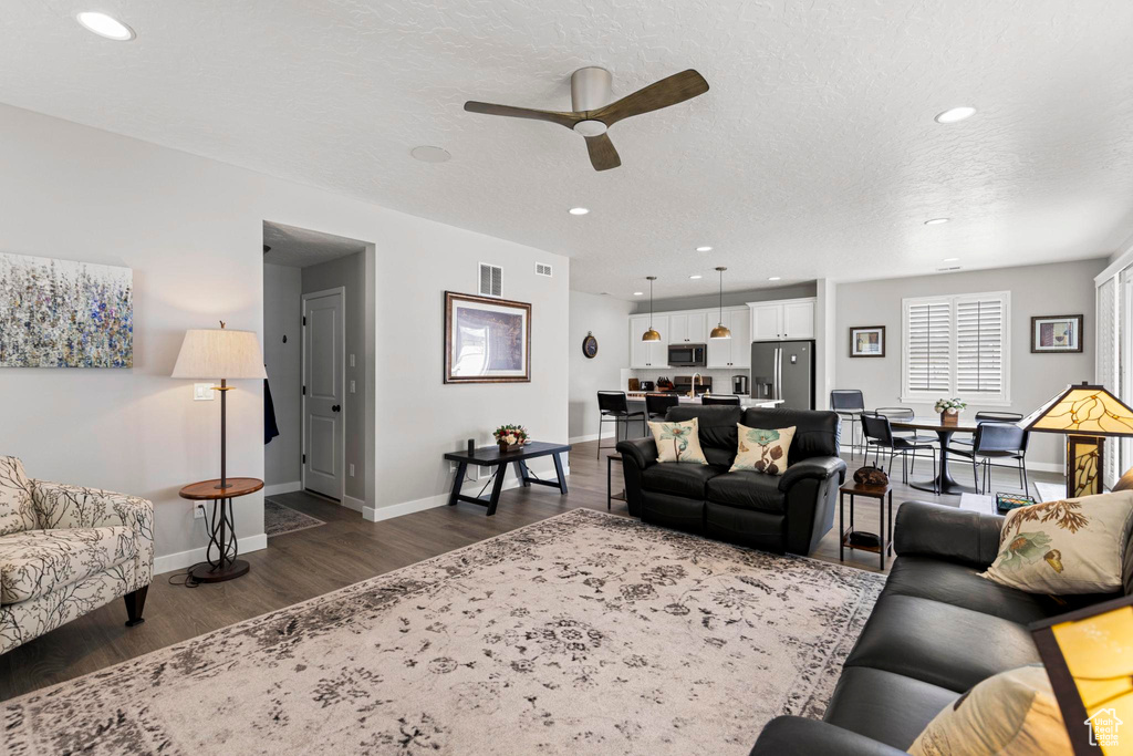 Living room with baseboards, ceiling fan, recessed lighting, a textured ceiling, and dark wood-style flooring